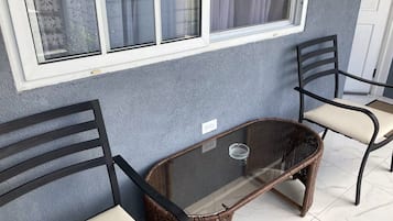 A room with two wicker chairs, a glass table, and a window with curtains.