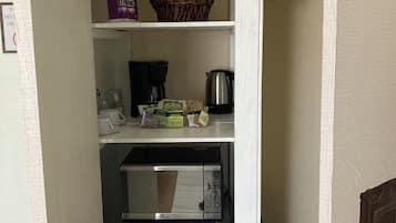 A compact kitchen with a refrigerator, coffee maker, tea bags, and a basket of groceries.