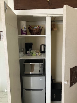 A compact kitchen with a refrigerator, coffee maker, tea bags, and a basket of groceries. - The Chique Suite - The Ultimate Urban Retreat (Kingston)