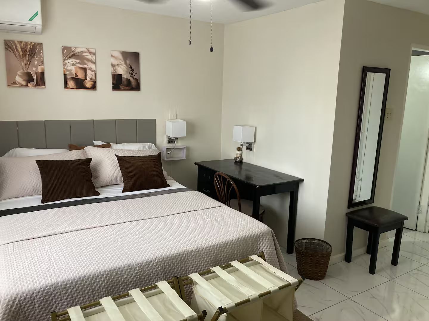 A hotel room with a bed, bedside tables, a desk, a chair, a mirror, and a waste basket.