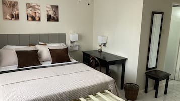 A hotel room with a bed, bedside tables, a desk, a chair, a mirror, and a waste basket.