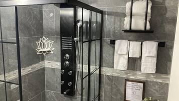 Een moderne badkamer met een douchecabine van glas, marmeren tegels, een lotusvormige decoratie en een bordje waarop staat dat er alleen toiletpapier doorspoeld mag worden.