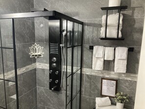 Un baño moderno con ducha envuelta en vidrio, baldosas de mármol, una decoración con forma de loto y un cartel que prohíbe arrojar nada más que papel higiénico.