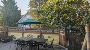 An outdoor patio with a table and chairs, a green umbrella, and a wooden fence.