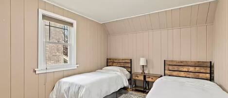 A bedroom with two beds, a window, a nightstand, and a ceiling light.