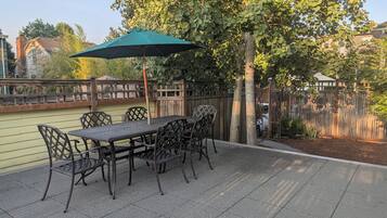 Een terras buiten met een tafel, stoelen, een groene parasol en een houten schutting.