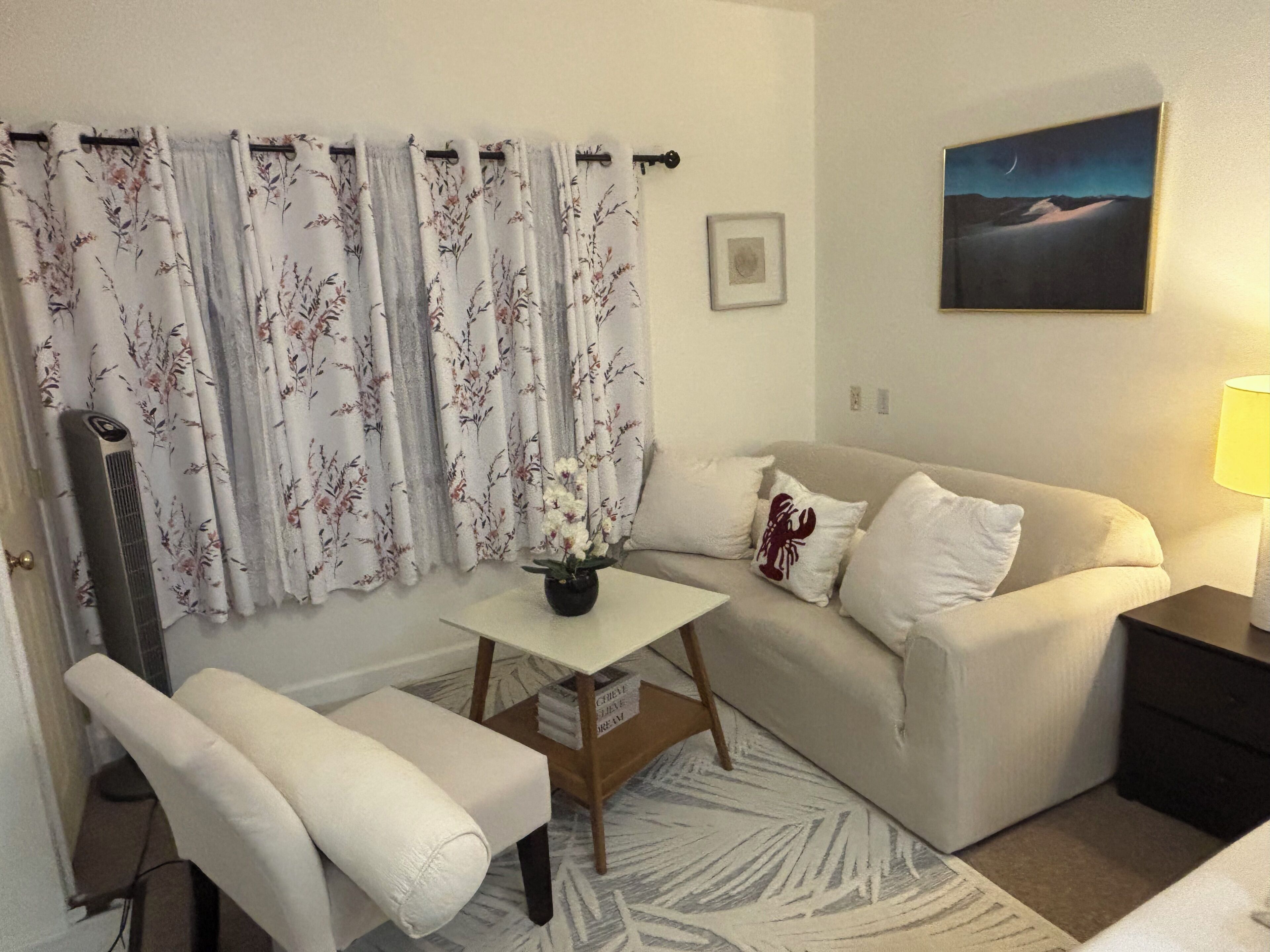 A living room with a sofa, a small table with a vase, a chair, a lamp, and a painting on the wall.