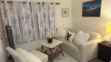 A living room with a sofa, a small table with a vase, a chair, a lamp, and a painting on the wall.