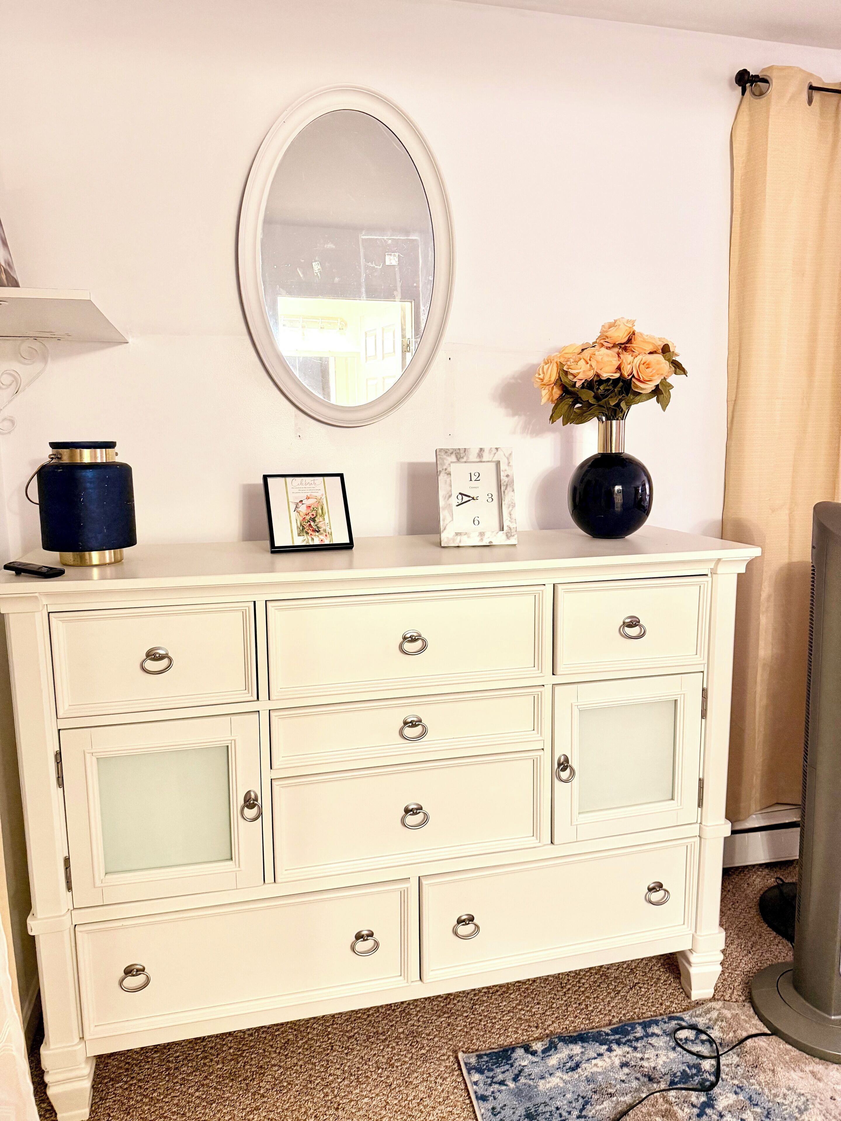 A white dresser with a mirror, a vase with flowers, and a framed picture.
