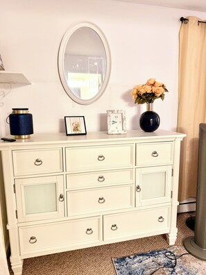 Une commode blanche avec un miroir, un vase de fleurs et un tableau encadré.