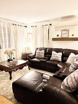 A living room with a leather sofa, a glass coffee table, and a rug.