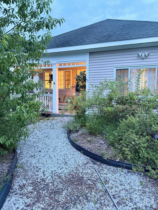 A house with a porch, a gravel pathway, and a variety of plants.