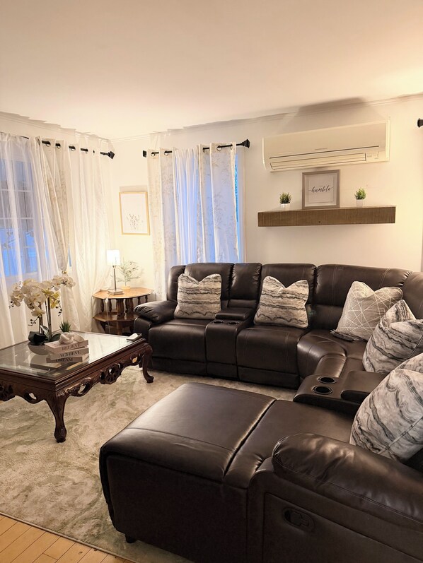 A living room with a leather sectional sofa, a glass coffee table, and a wooden side table.