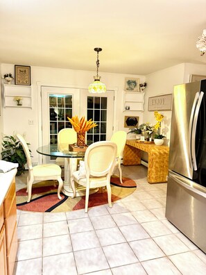 A kitchen with a dining table, chairs, a refrigerator, and a hanging light fixture.