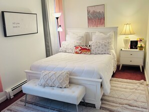 Une chambre à coucher bien rangée, avec un lit, des tables de chevet, un banc et un tableau accroché au mur.