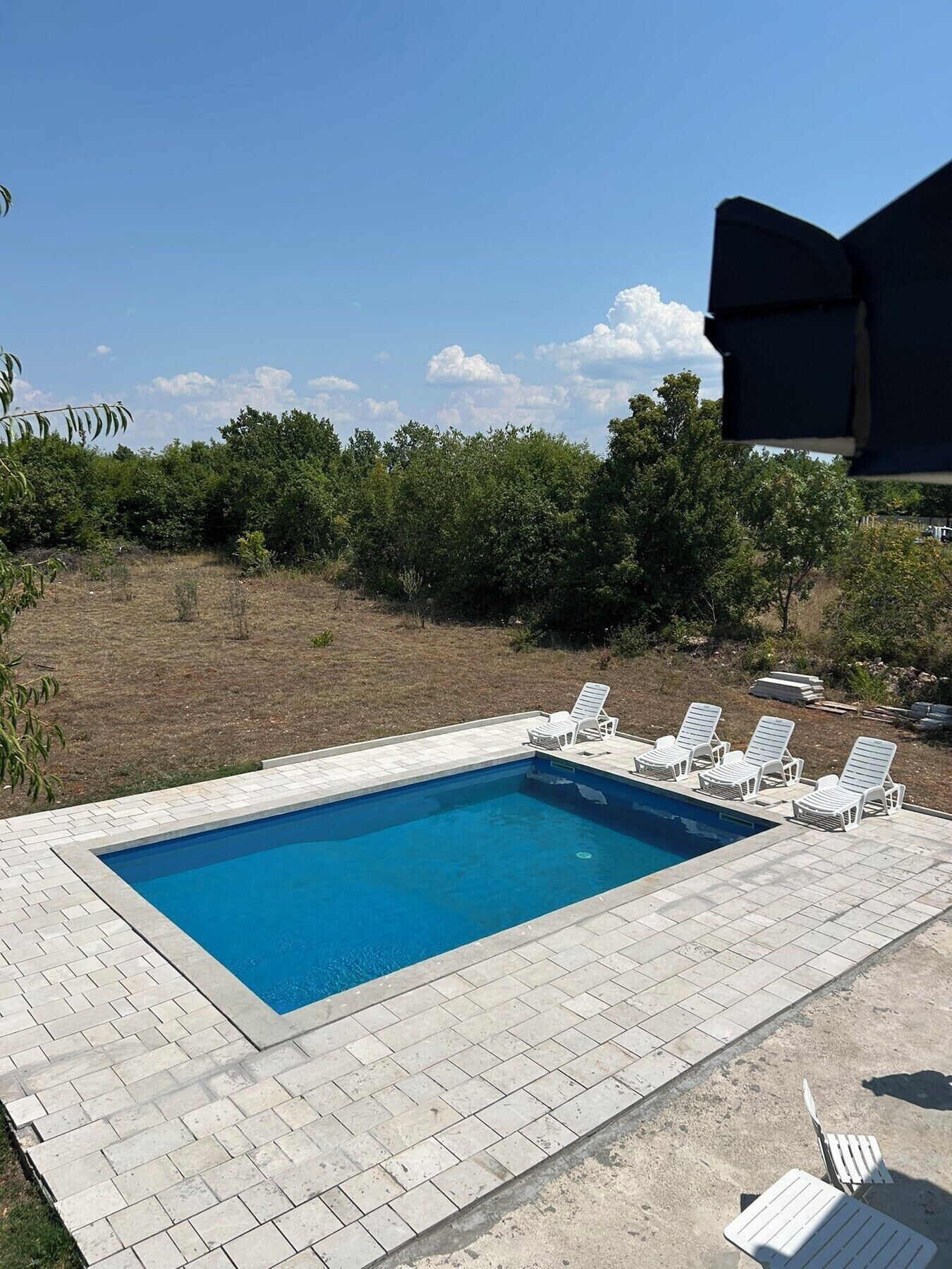 Una piscina rectangular con un borde empedrado, rodeada de sillones blancos.