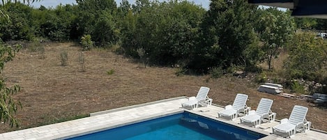 Una piscina rettangolare con bordo piastrellato, circondata da poltrone da relax bianche.