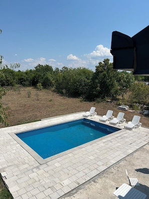 A rectangular swimming pool with a tiled deck, surrounded by white lounge chairs.
