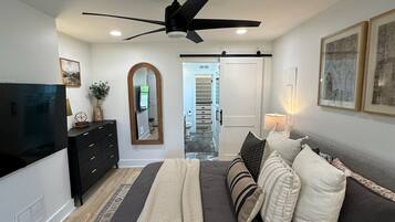 Een slaapkamer met een bed, een dresser, een televisie, een plafondventilator en een deur naar een badkamer.