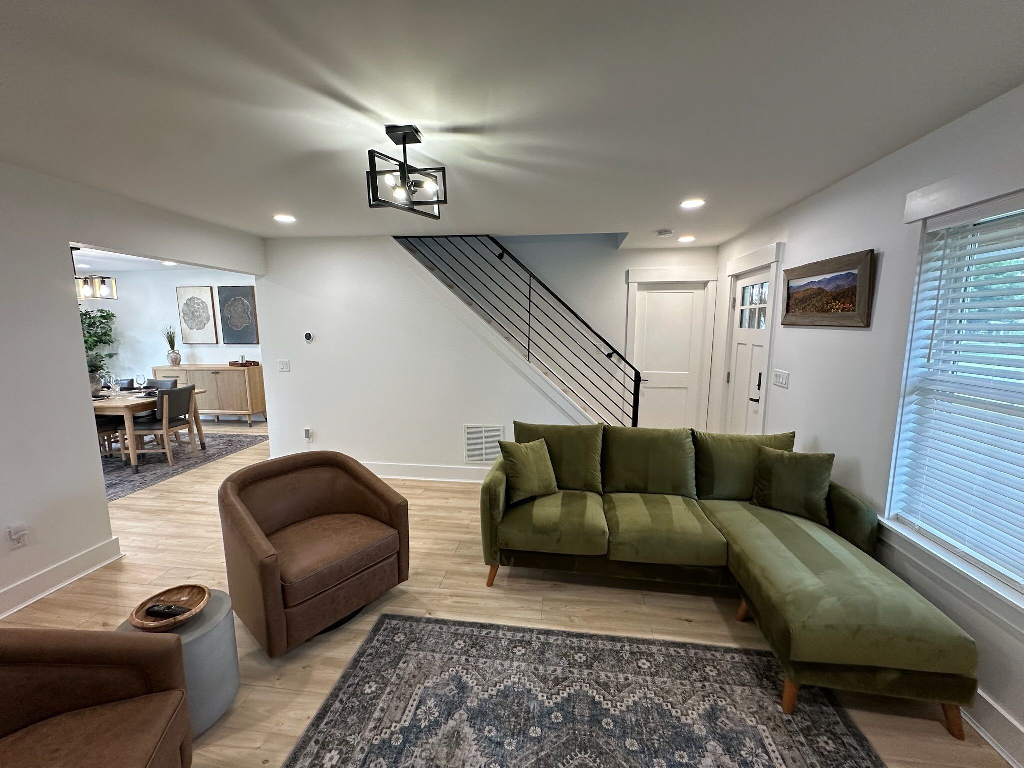 Una sala de estar moderna con un sofá seccional, un sillón marrón y un tapete estampado. Una escalera conduce a un nivel superior.