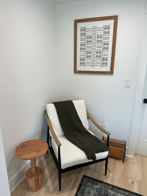 Ein moderner Stuhl mit weißem Kissen und dunkler Decke, platziert neben einem kleinen Holztisch.