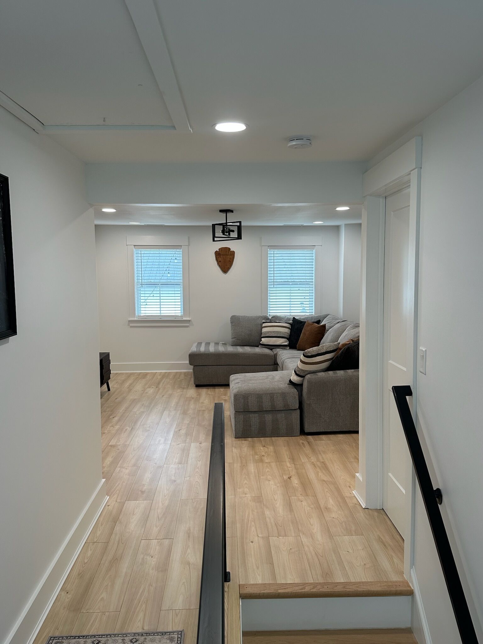 Ein modernes Wohnzimmer mit einem grauen Ecksofa, Holzboden und einer Treppe, die in eine obere Etage führt.
