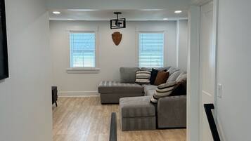 Ein modernes Wohnzimmer mit einem grauen Ecksofa, Holzboden und einer Treppe, die in eine obere Etage führt.
