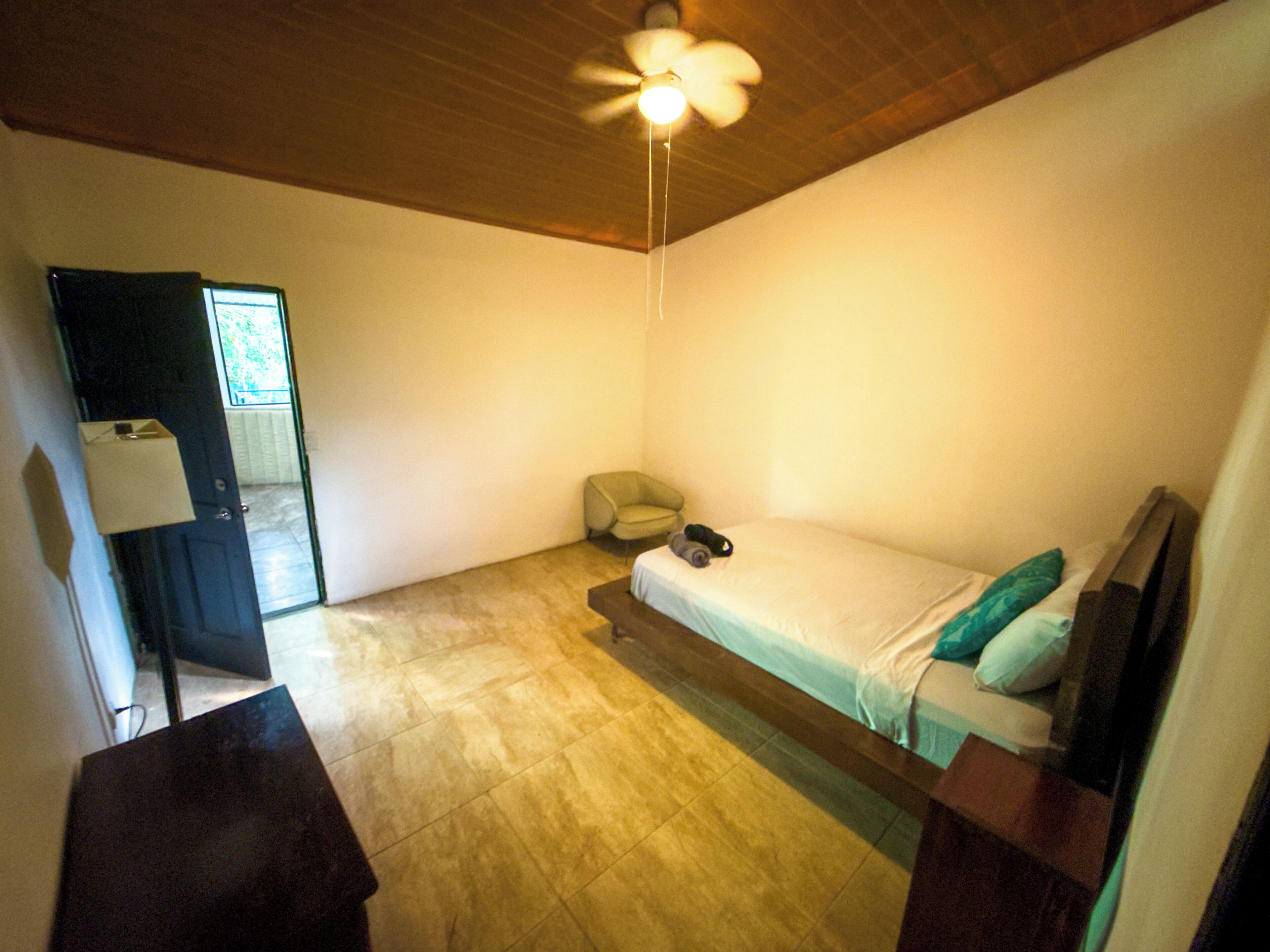 A bedroom with a bed, a chair, a desk, and a ceiling fan.