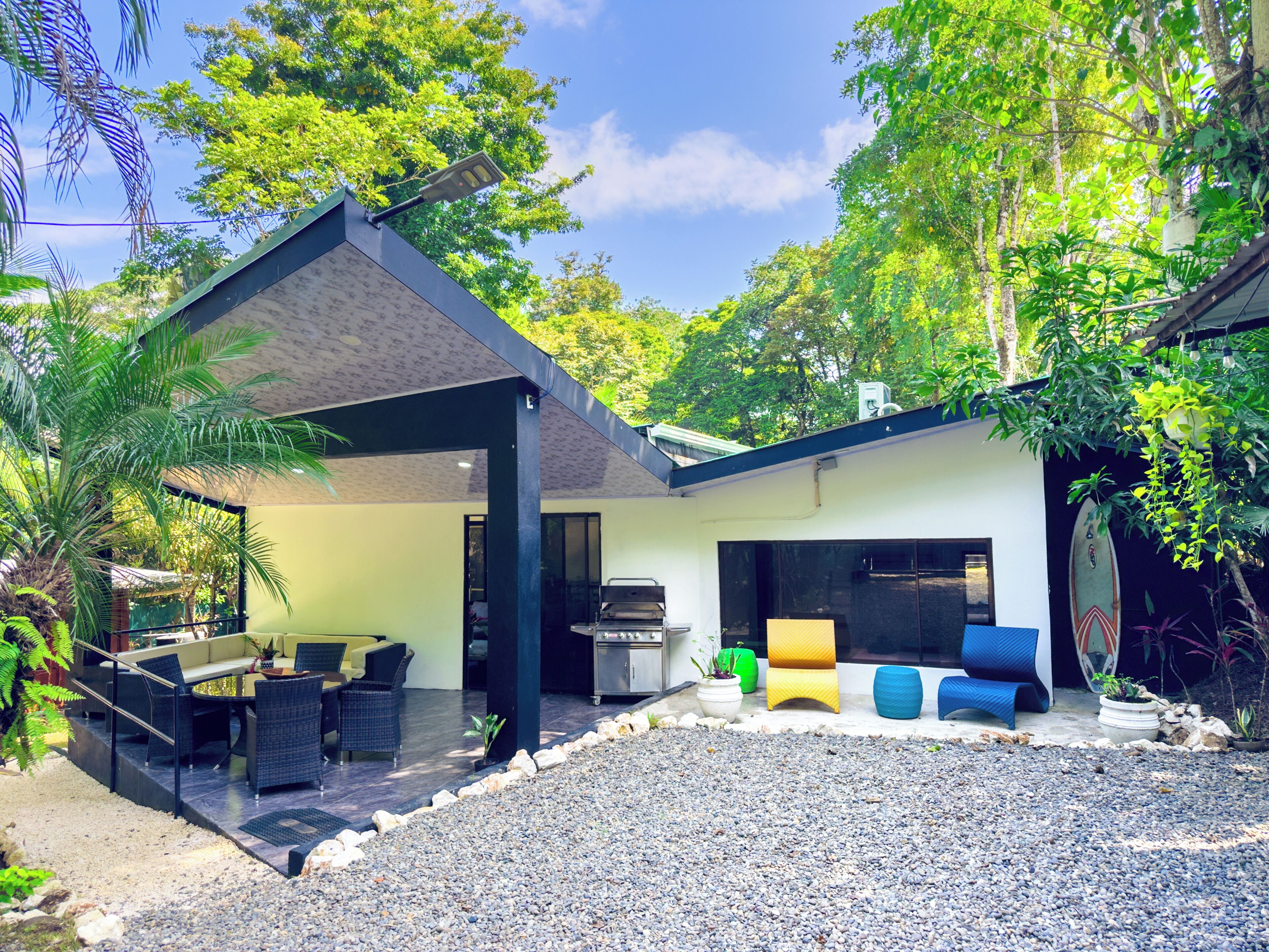An outdoor patio area with a covered seating area, a grill, and a surfboard.