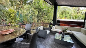 An outdoor seating area with wicker furniture, a glass table, and a view of lush greenery. - Mountain House,Beautiful 3-bedroom with AC in quaint Puerto Viejo de Talamanca (Puerto Viejo de Talamanca)