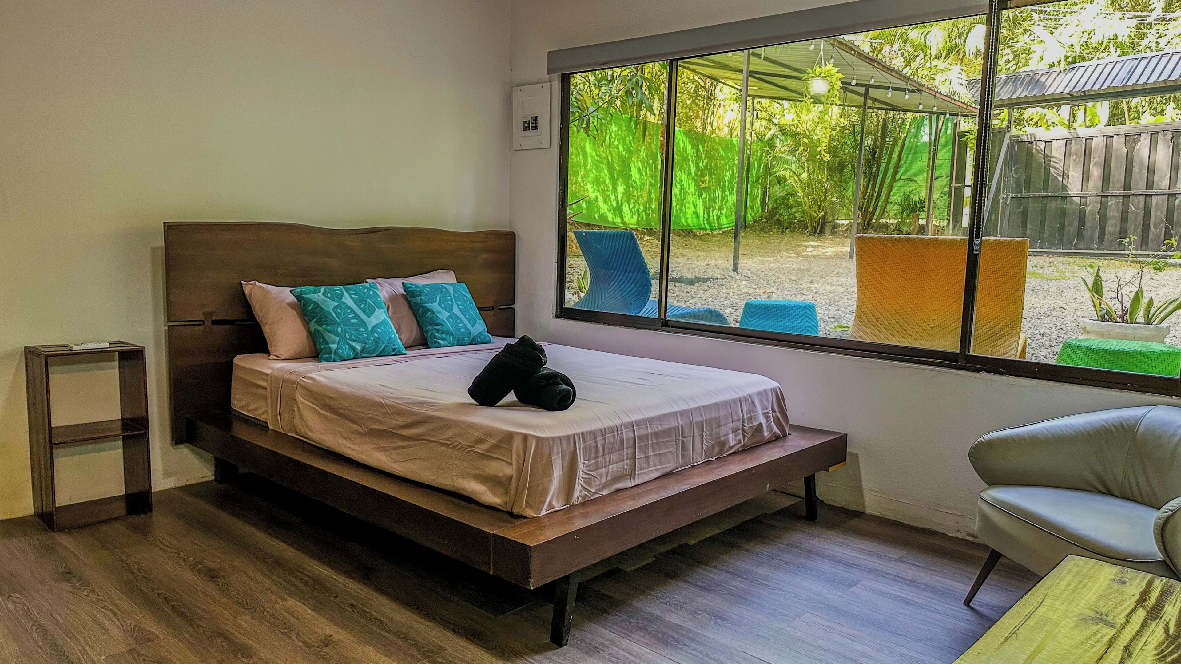 Ein Schlafzimmer mit einem Bett, einem Nachttisch, einem Stuhl und einem großen Fenster mit Blick ins Freie.