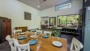 A dining area with a wooden table set for four, surrounded by white chairs, and a kitchen area with a large window. - Mountain House,Beautiful 3-bedroom with AC in quaint Puerto Viejo de Talamanca (Puerto Viejo de Talamanca)