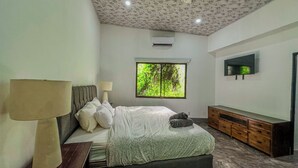 A bedroom with a bed, a TV, a window with a view of trees, and a ceiling with a floral pattern. - Mountain House,Beautiful 3-bedroom with AC in quaint Puerto Viejo de Talamanca (Puerto Viejo de Talamanca)