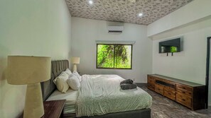 Ein Schlafzimmer mit einem Bett, einem Fernseher, einem Fenster mit Blick auf Bäume und einer Decke mit floralem Muster.