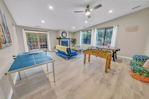 Una habitación con mesa de ping pong, mesa de futbolín, un sofá azul y ventilador de techo.