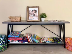 Ein Tisch mit einem gerahmten Bild, einem Korb, einer Topfpflanze sowie verschiedenen Gesellschaftsspielen und Büchern.