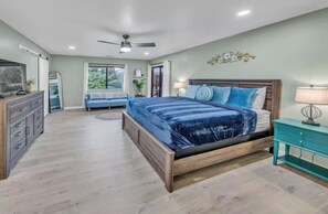 Une chambre à coucher avec un grand lit, une table de chevet, une commode et un ventilateur de plafond.