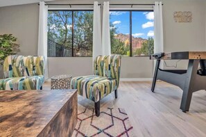 A room with a large window, two striped armchairs, a coffee table, and a wooden side table. - Luxury Red Rock Retreat with Hot Tub, Fire Pit, Game Room and Large Yard (Sedona)