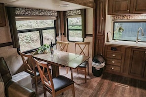 A compact kitchen with a dining area, a sink, and a window with a view of greenery. - Forest Glamping Getaway with King Bed, Deck, and Cozy Fireplace (Dallas)