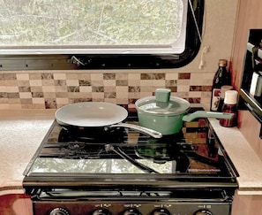 A kitchen with a gas stove, a frying pan, a pot with a lid, and a range hood. - Forest Glamping Getaway with King Bed, Deck, and Cozy Fireplace (Dallas)