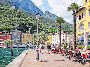 Eine Uferpromenade mit Gebäuden, einer Laterne und Personen, die an Tischen im Freien essen.