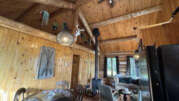 A rustic cabin interior with a dining area, a living room with a sofa, and a kitchen area.