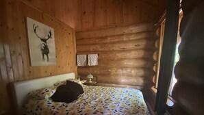 Una habitación de cabaña de madera con una cama, un cuadro colgado en la pared y una ventana.