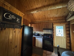 A wooden interior with a kitchen area featuring a refrigerator, stove, and microwave. - The Big Pine Shelter (Saint-Gabriel-de-Valcartier)