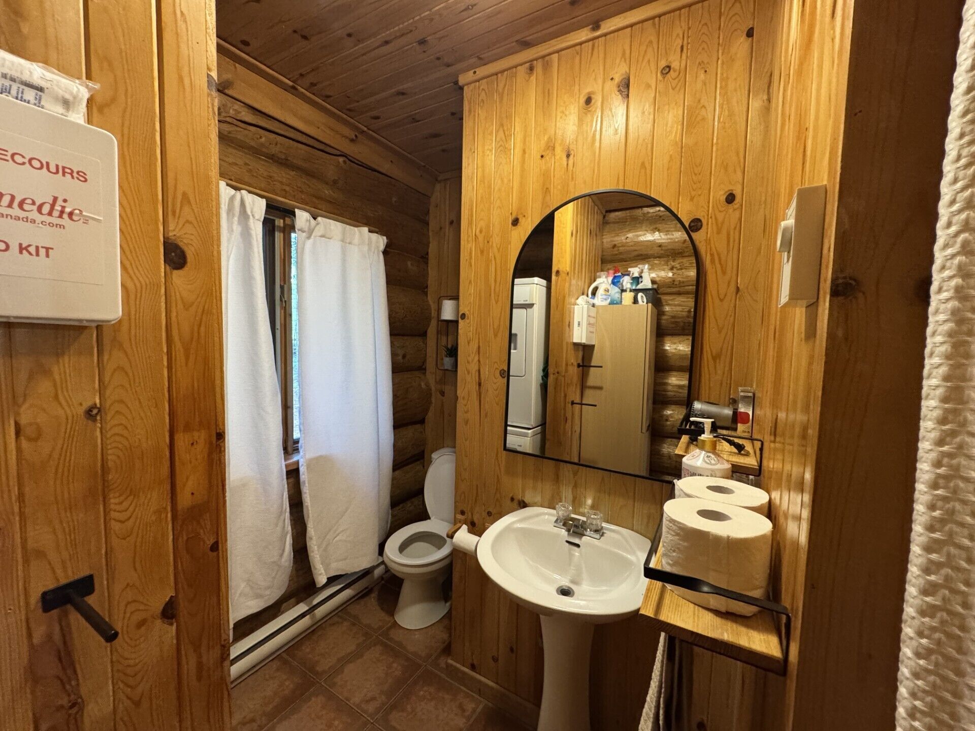A wooden cabin bathroom with a toilet, sink, and shower curtain.