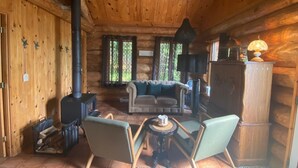 Interior de una cabaña de troncos con chimenea, zona de estar y una lámpara.