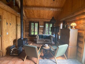 A log cabin interior with a fireplace, seating area, and a lamp. - The Big Pine Shelter (Saint-Gabriel-de-Valcartier)