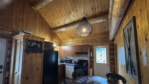 Interior de madera con una mesa de comedor, sillas, un refrigerador y una cocina que incluye estufa y fregadero.