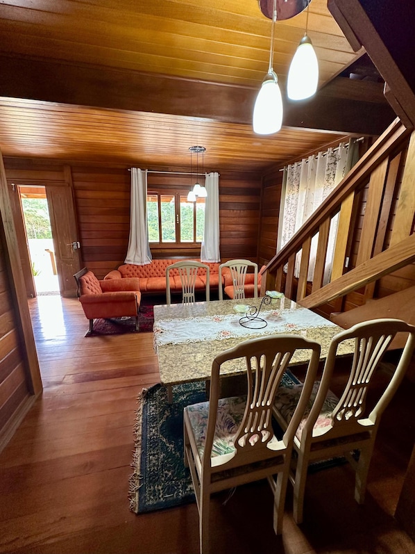 A wooden interior with a dining table, chairs, a sofa, and a staircase.