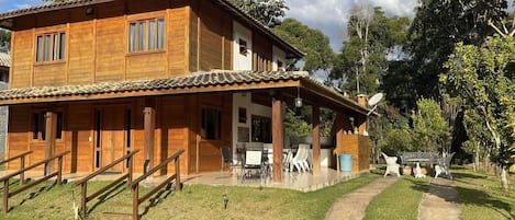 Un edificio de madera de dos pisos con un porche cubierto, mesas al aire libre y un sendero que lleva a la entrada.